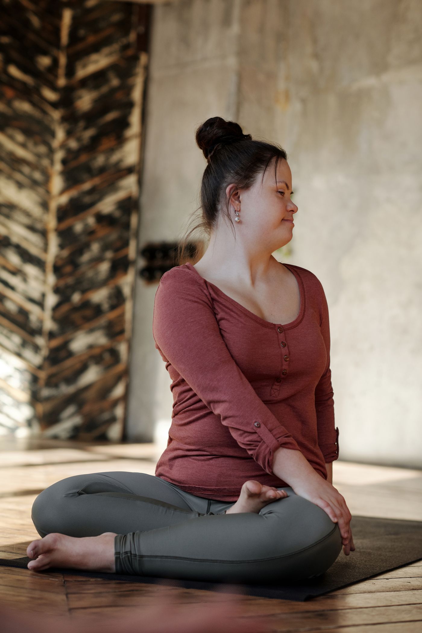 A woman seated on a yoga mat practicing a gentle stretch indoors