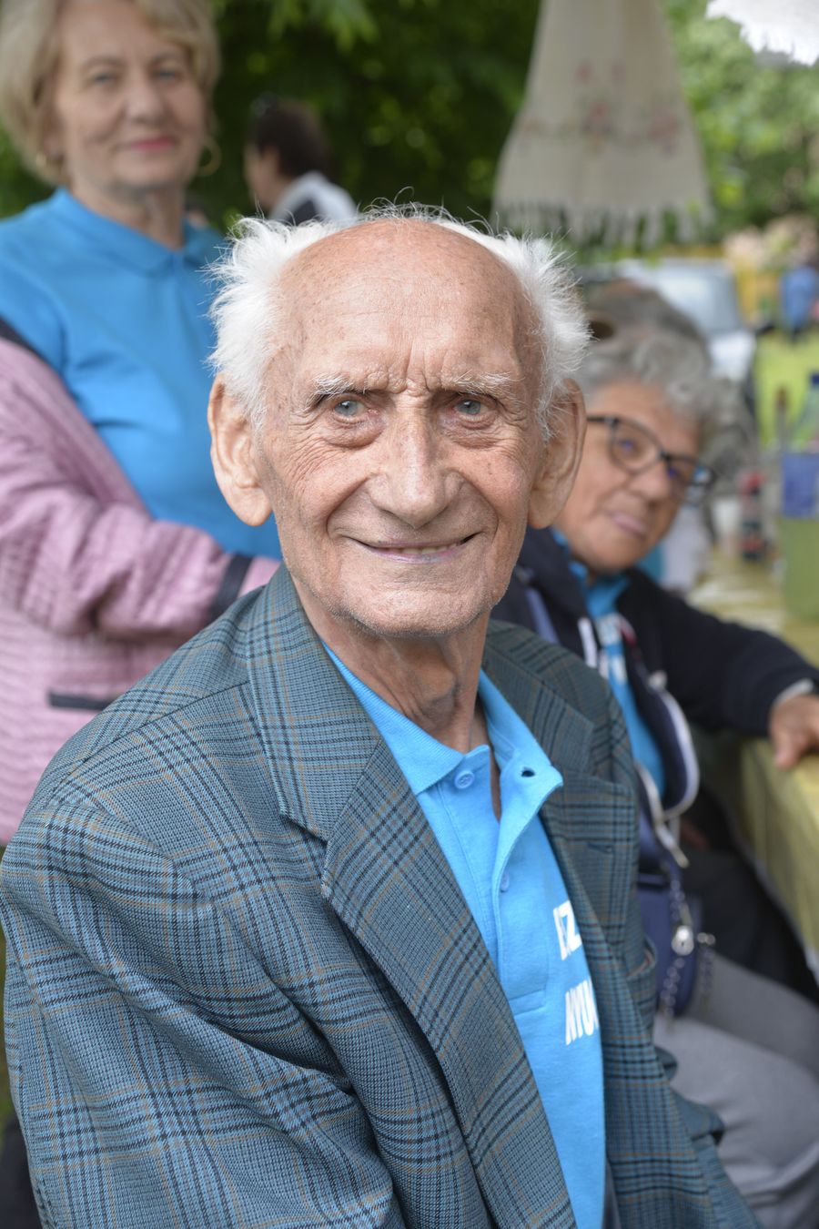 Older adults gathered outdoors, with a smiling man seated in the foreground